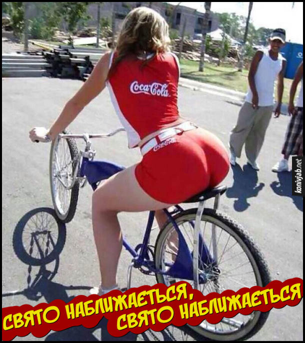 Новорічна реклама. Дівчина з великою дупою їде на велосипеді в в фірмовому костюмі Coca-Cola. Свято наближається, свято наближається