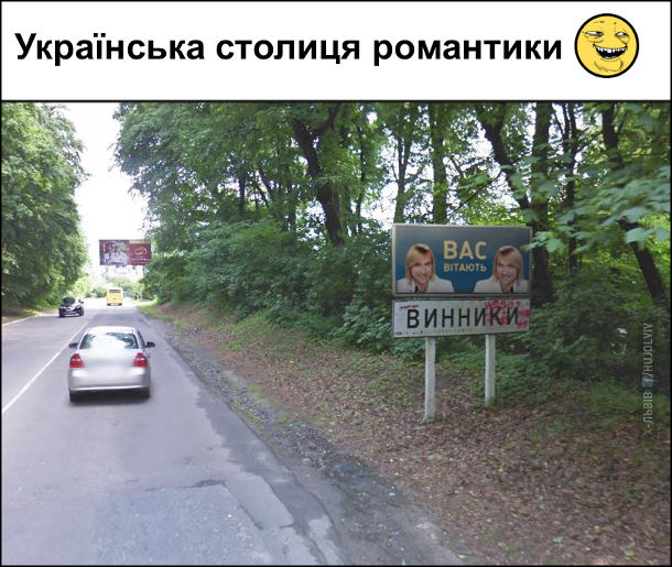 Українська столиця романтики. Дорожній знак місто Винники, Львівської області, а над знаком банер, де два Олега Винника